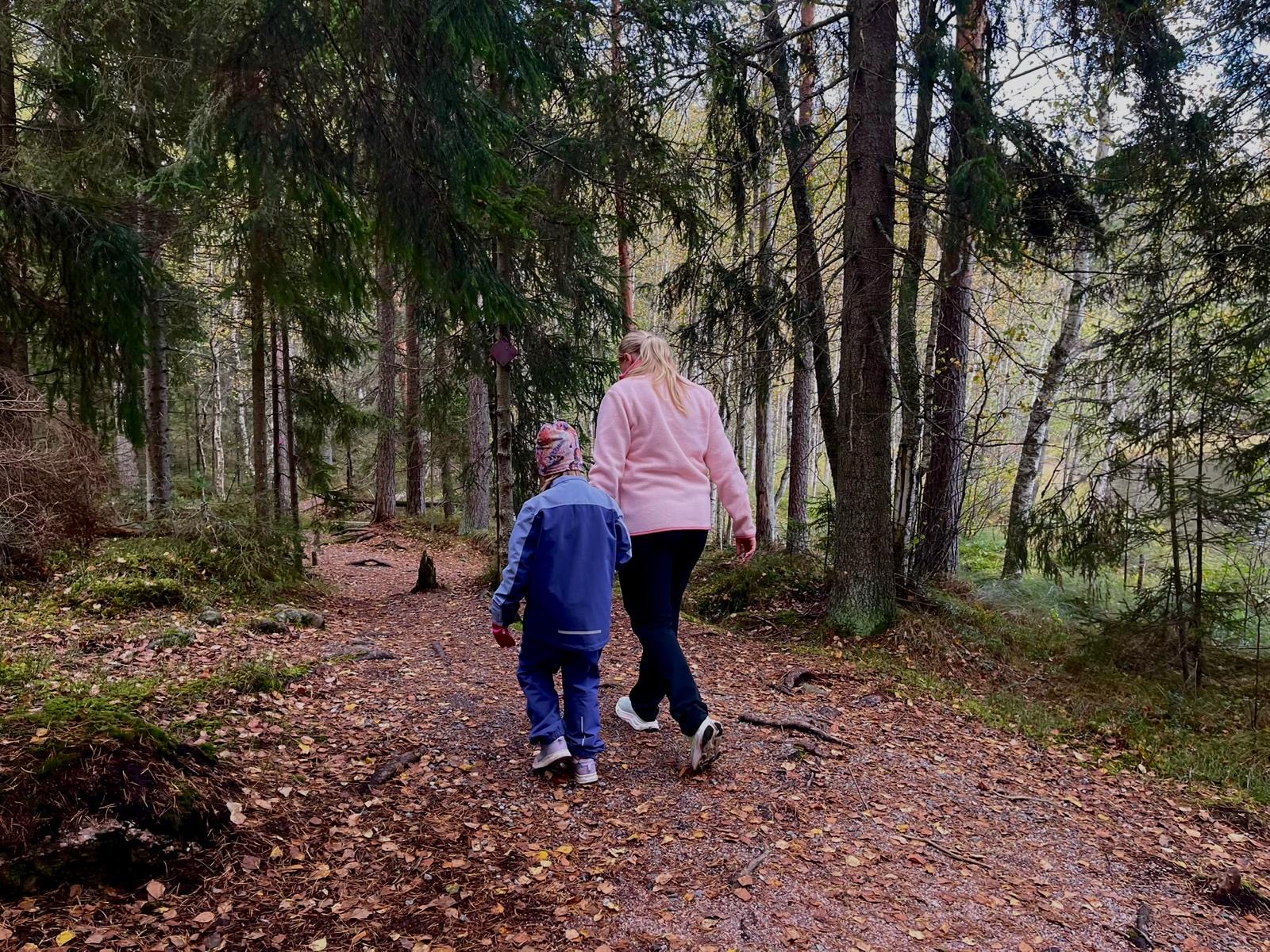 Lastenvahti kävelee lapsen kanssa metsäpolulla